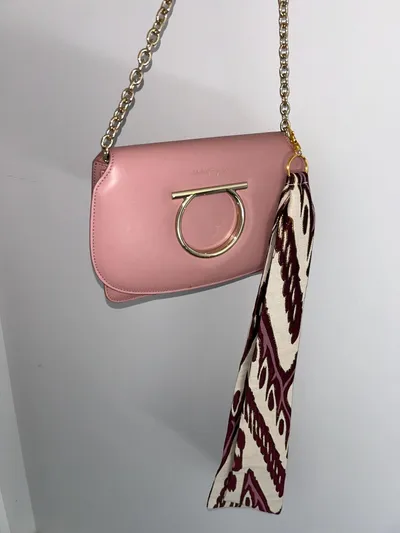 Pink leather bag with the atlas ikat ribbon charm clasped to its gold chain, hanging against a plain wall