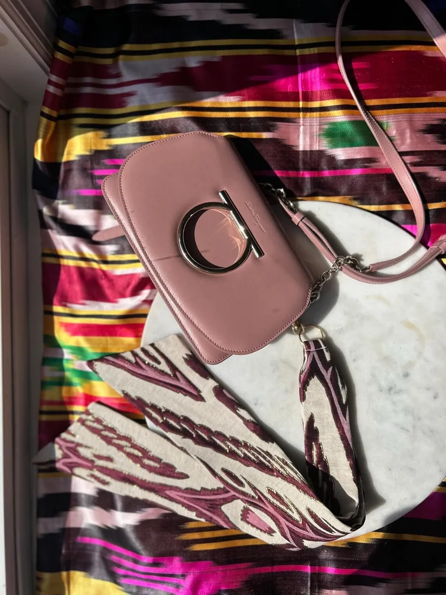 Flat lay of the pink bag and untied ikat ribbon on a marble round, with colorful striped ikat fabric in the background