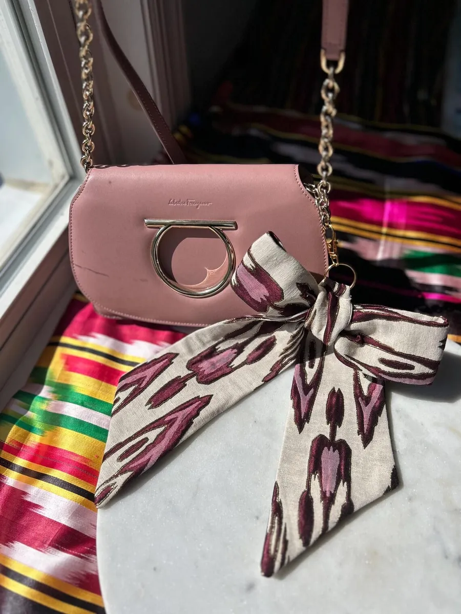 Atlas ikat bag charm clipped to the chain strap of a pink crossbody bag worn over the shoulder