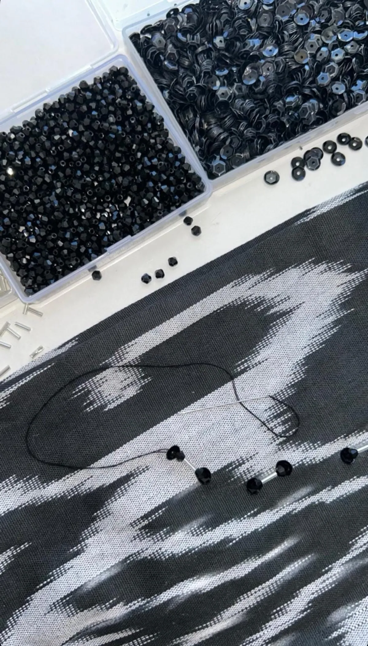 Black glass beads, sequins, and thread laid out on dark atlas ikat silk, mid-embellishment for a custom baska