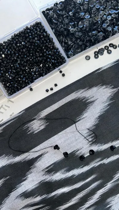 Black glass beads, sequins, and thread laid out on dark atlas ikat silk, mid-embellishment for a custom baska