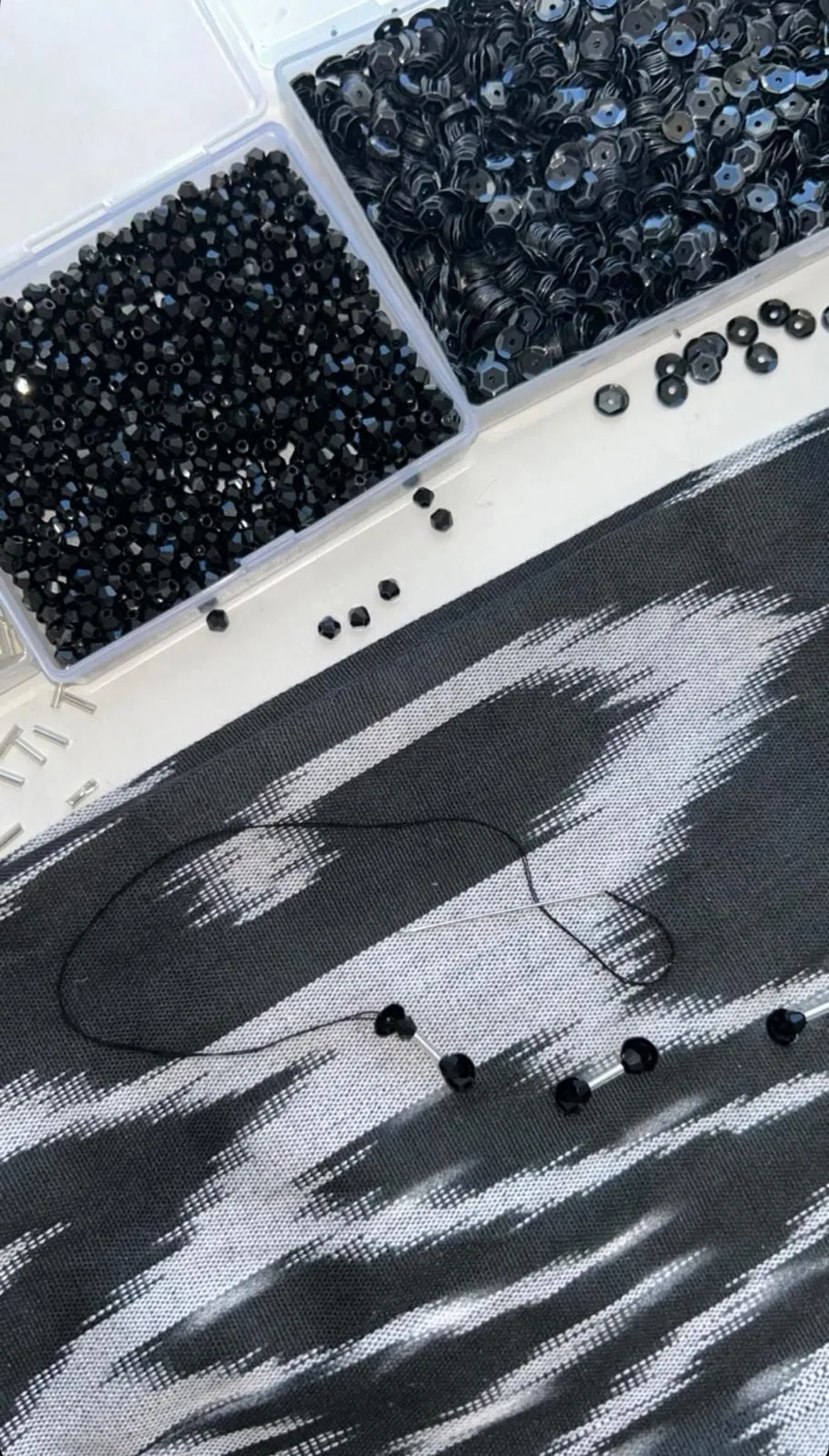 Black glass beads, sequins, and thread laid out on dark atlas ikat silk, mid-embellishment for a custom baska