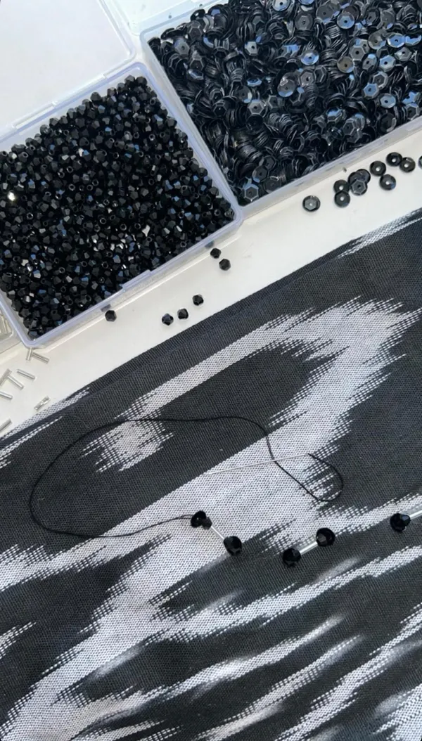 Black glass beads, sequins, and thread laid out on dark atlas ikat silk, mid-embellishment for a custom baska