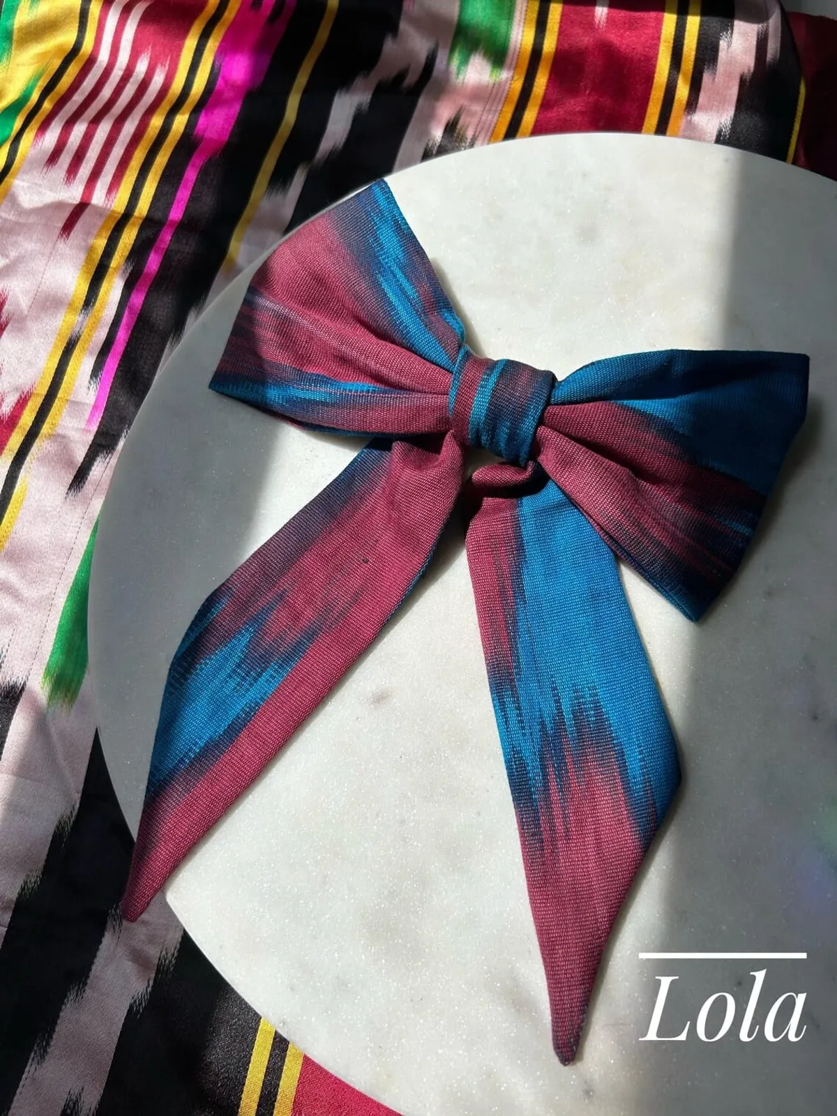 Atlas ikat hair bow in pink, blue, and navy tones tied on a marble surface