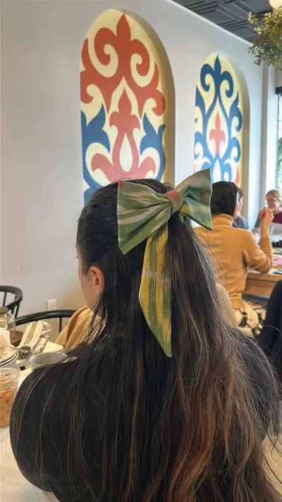 Atlas ikat hair bow in green, yellow, and pink tones worn in a ponytail