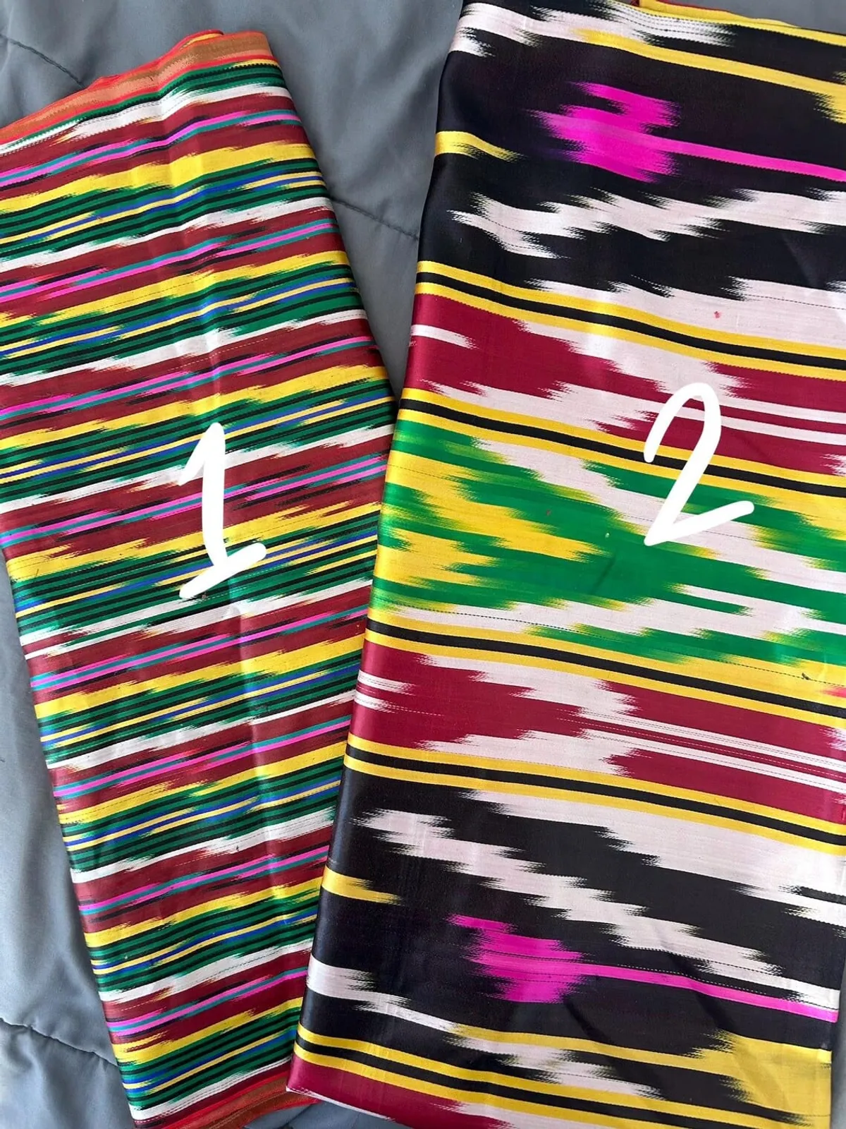 Two folded bolts of striped multicolor ikat silk fabric
