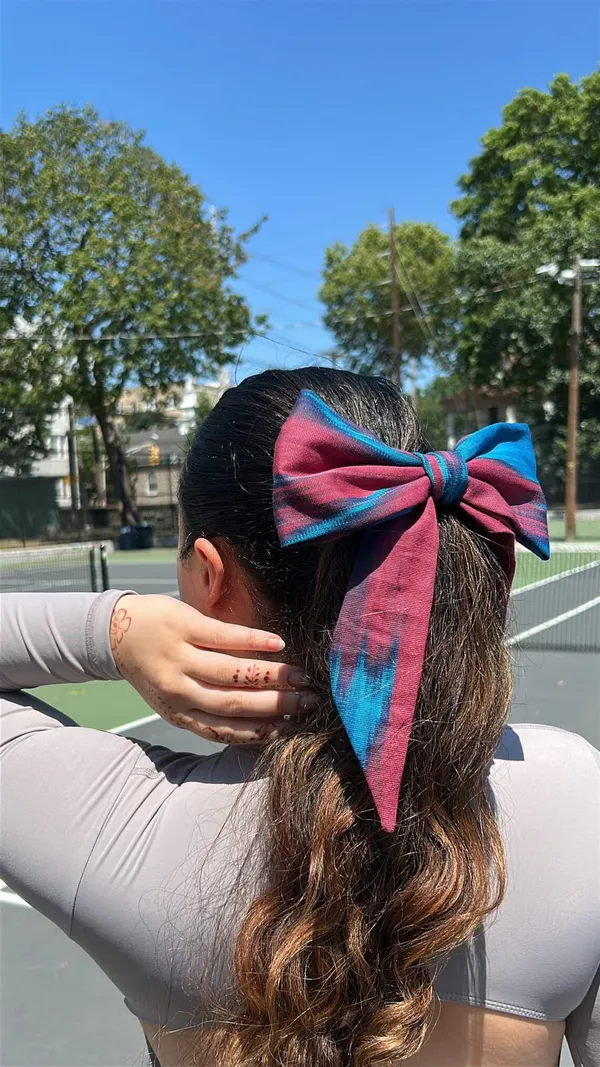 Atlas ikat hair bow in pink and blue tones worn in a low ponytail outdoors