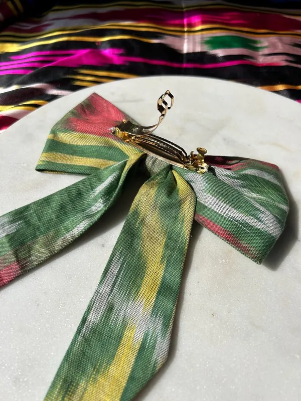 A red, green, and yellow atlas ikat silk hair bow with a gold alligator clip