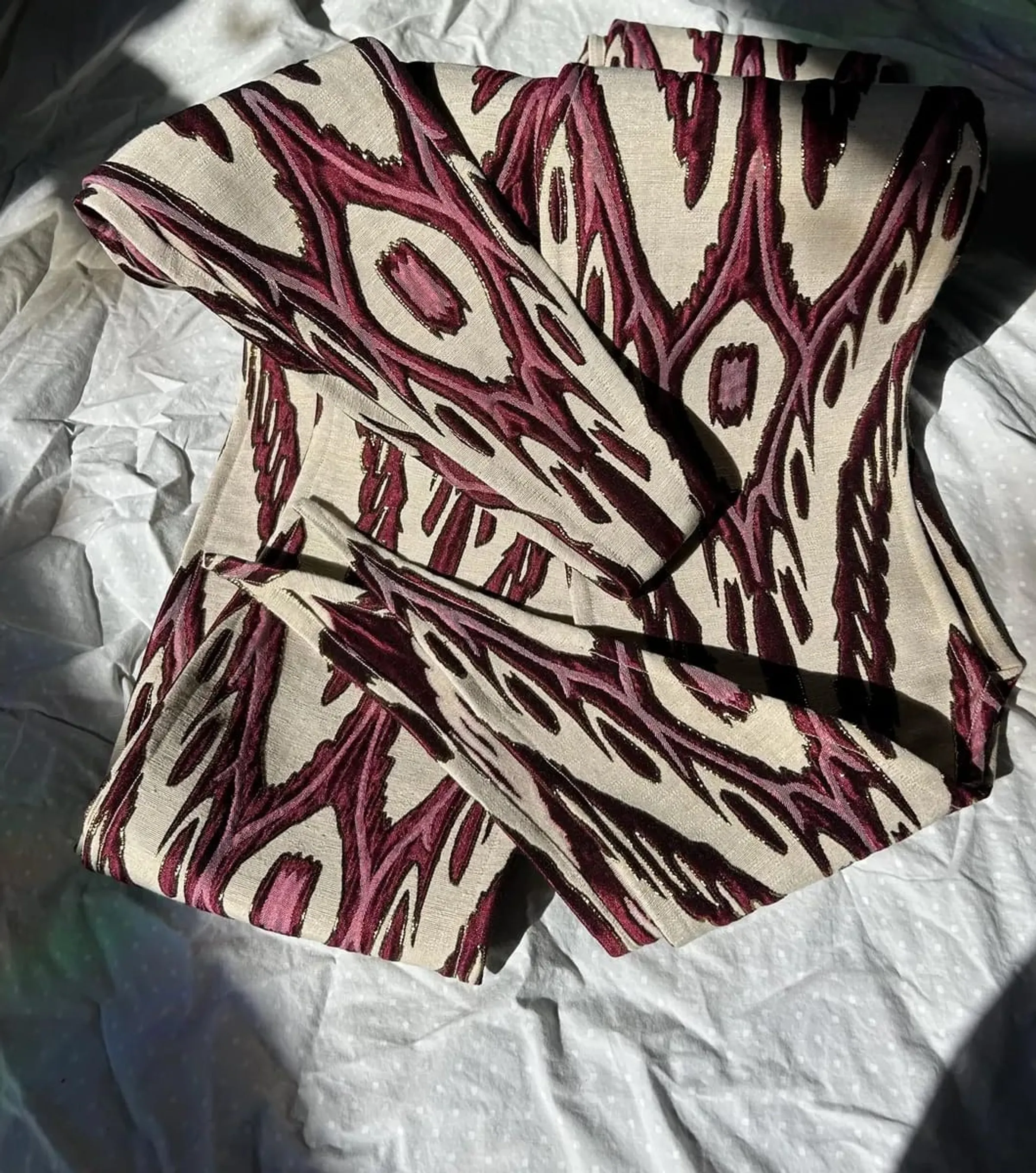 Macro close-up of burgundy, cream, and gold atlas ikat silk, showing the feathered edge of the dye pattern