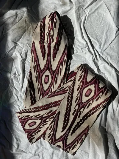 An atlas ikat silk neck scarf laid flat in a burgundy and cream diamond ikat pattern with gold metallic threading