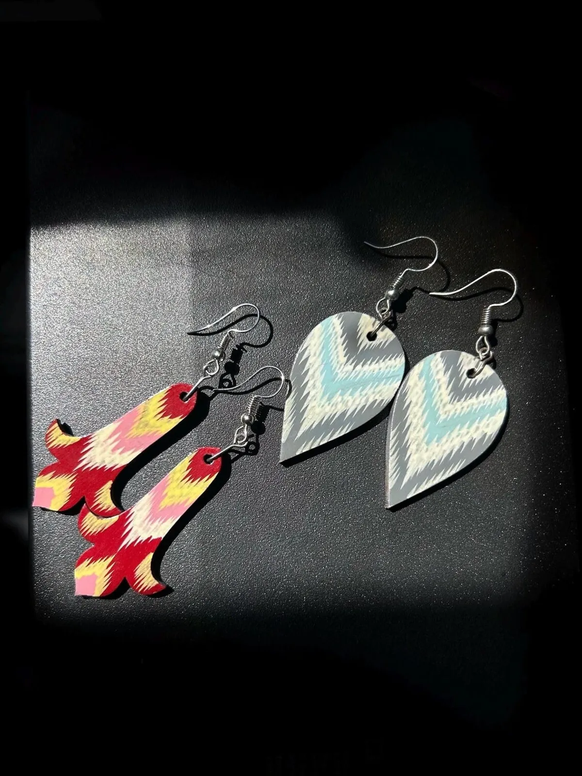 Two colorways of ikat-printed earrings side by side, one in red-yellow-pink and one in gray-cream-blue
