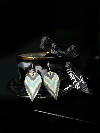 Gray, cream, and blue ikat-printed leaf-shaped earrings hanging from a vintage teacup with a Meros ribbon