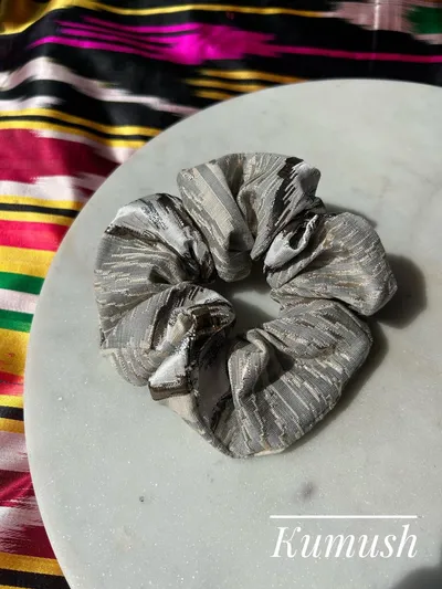 A metallic silver ikat scrunchie on a marble plate, labeled 'Kumush'