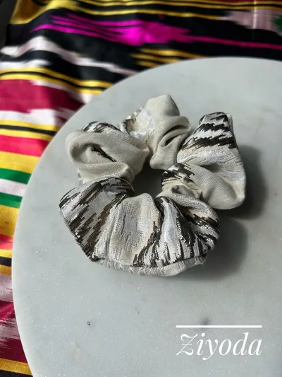 A silver and charcoal striped ikat scrunchie on a marble plate, labeled 'Ziyoda'