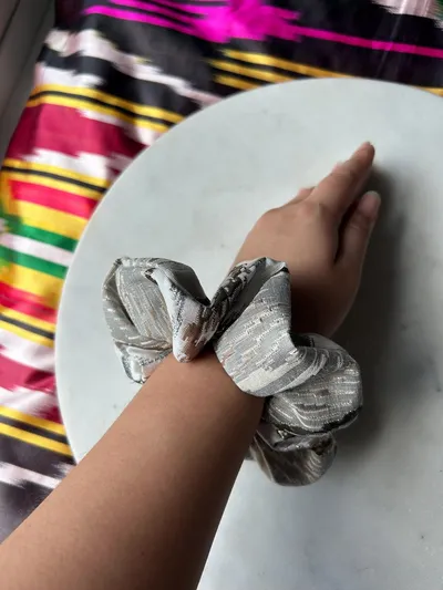 A metallic silver ikat scrunchie worn on a wrist