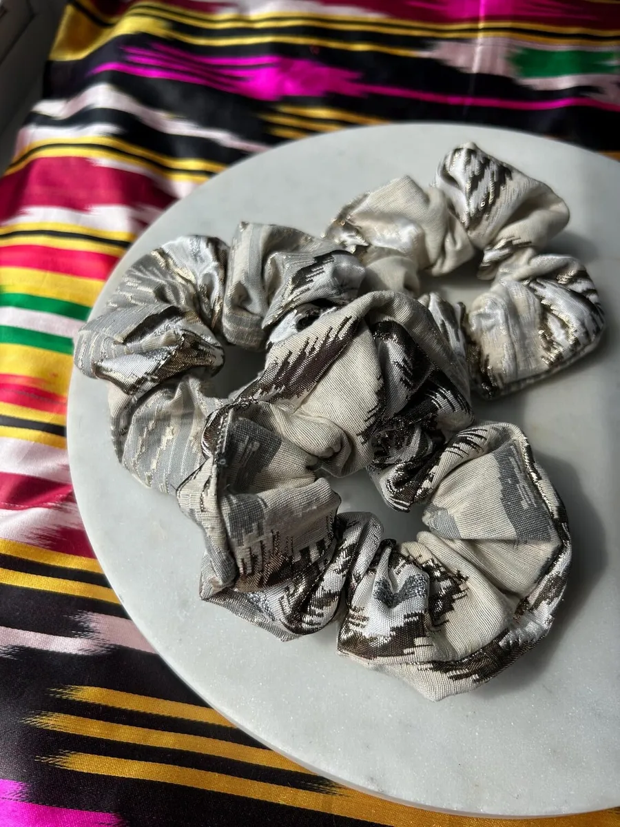 A metallic silver ikat scrunchie bunched on a marble plate
