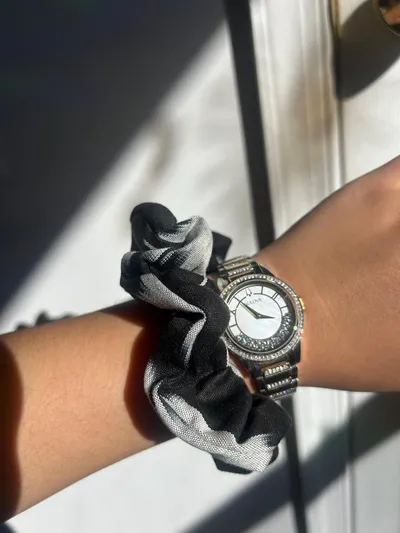 A black and white plaid ikat scrunchie worn on a wrist alongside a watch