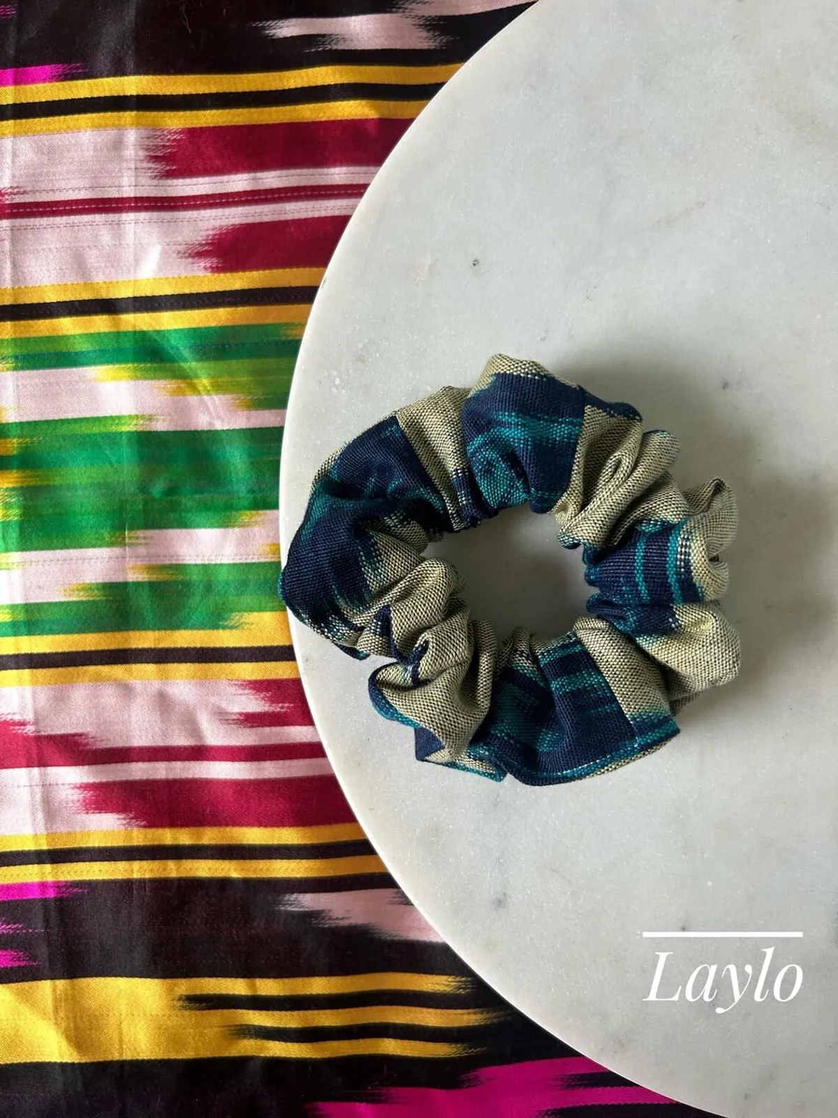 A navy, teal, and cream plaid ikat scrunchie on a marble plate, labeled 'Laylo'