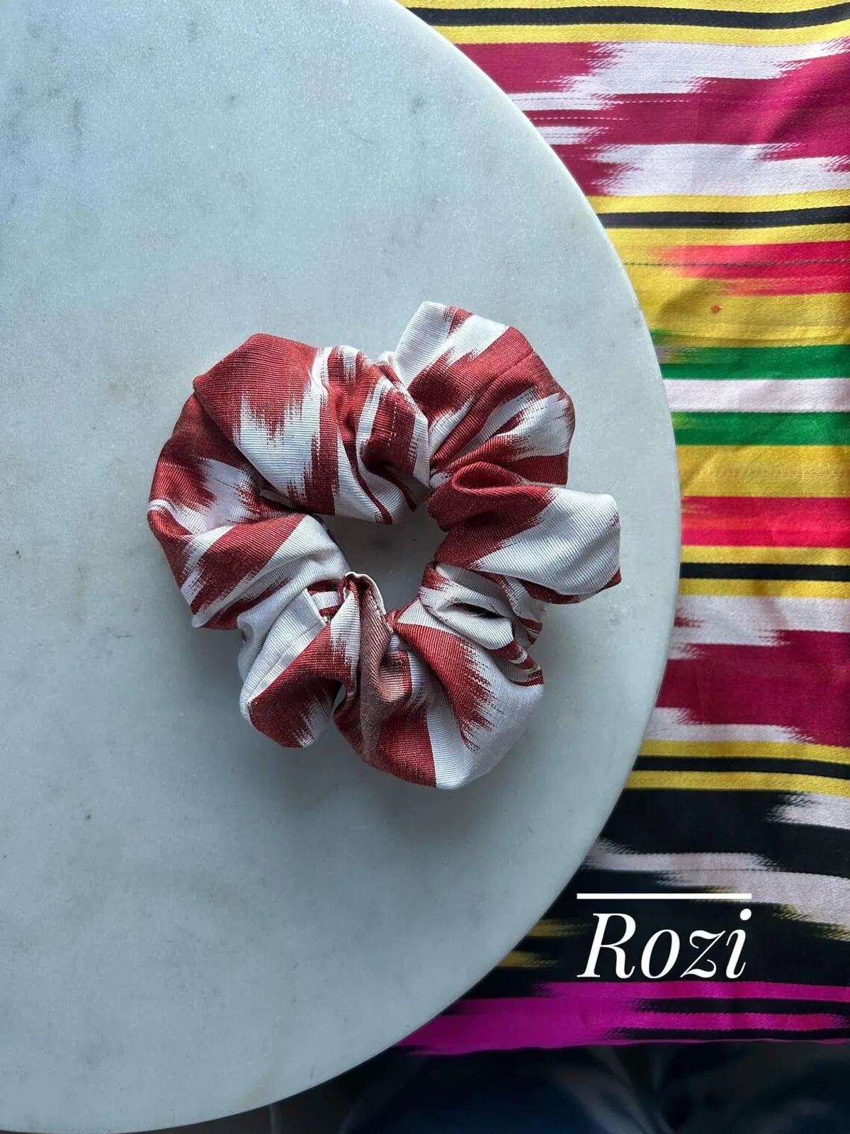 A red and white striped ikat scrunchie on a marble plate, labeled 'Rozi'