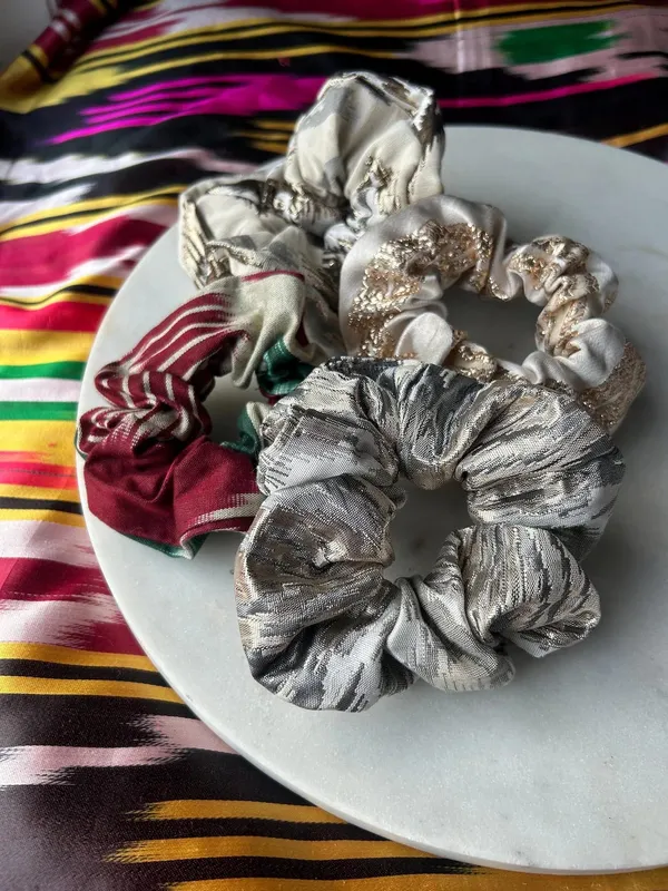 A pile of atlas ikat scrunchies in silver, red-and-white, and gold-embellished colorways on a marble plate
