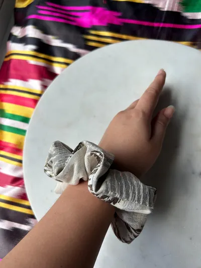 A metallic silver ikat scrunchie worn on a wrist, resting on a marble plate