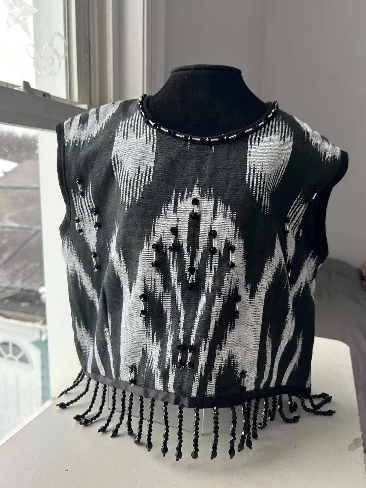 Black-and-white atlas ikat vest on a dress form, front view with beaded neckline and fringe hem