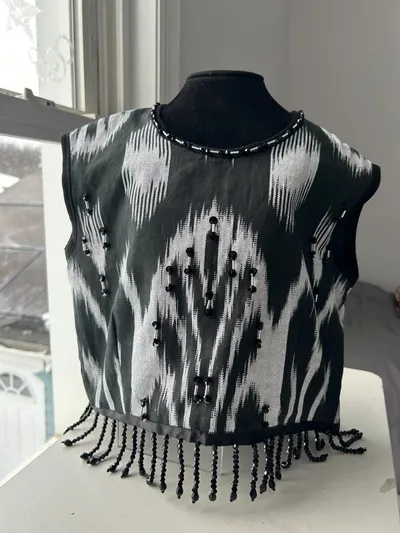 Black-and-white atlas ikat vest on a dress form, front view with beaded neckline and fringe hem