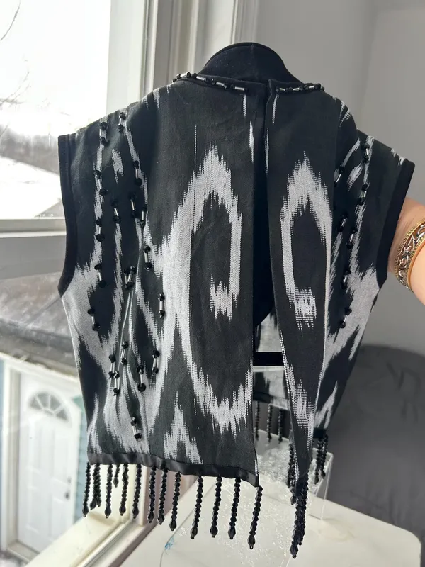 Black-and-white atlas ikat vest on a dress form, back view showing the open back and beaded fringe hem