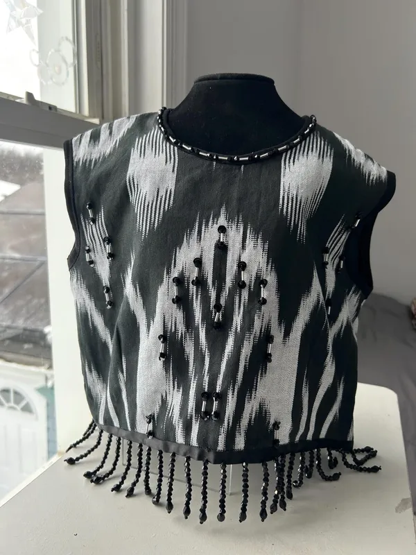 Black-and-white atlas ikat vest on a dress form, front view with beaded neckline and fringe hem