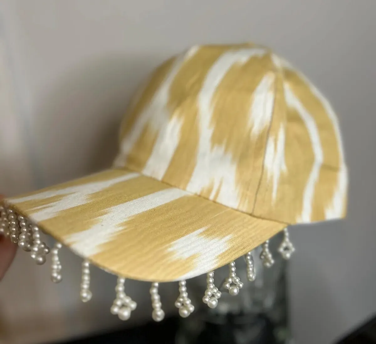 A gold and cream ikat baseball cap with pearl bead fringe along the brim