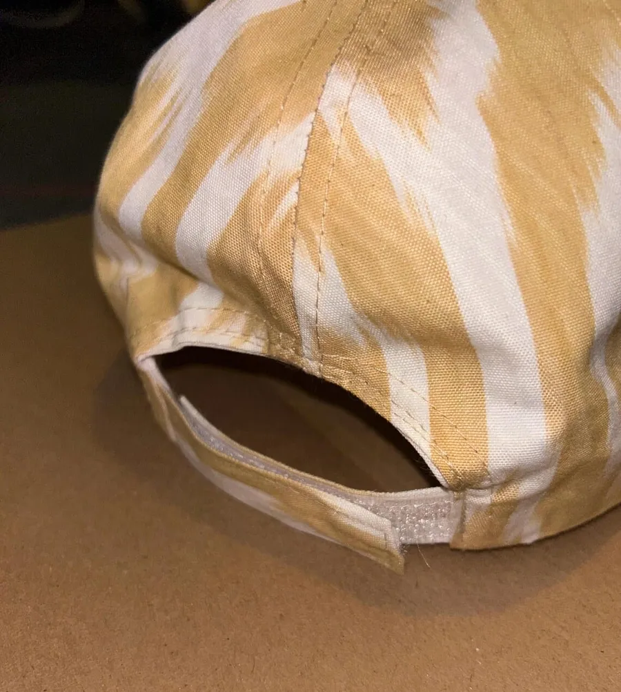 Back view of a gold and cream ikat baseball cap showing the adjustable strap