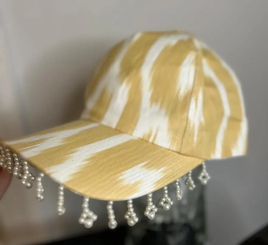 A gold and cream ikat baseball cap with pearl bead fringe along the brim
