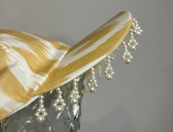 Close-up of pearl bead fringe along the brim of a gold and cream ikat baseball cap